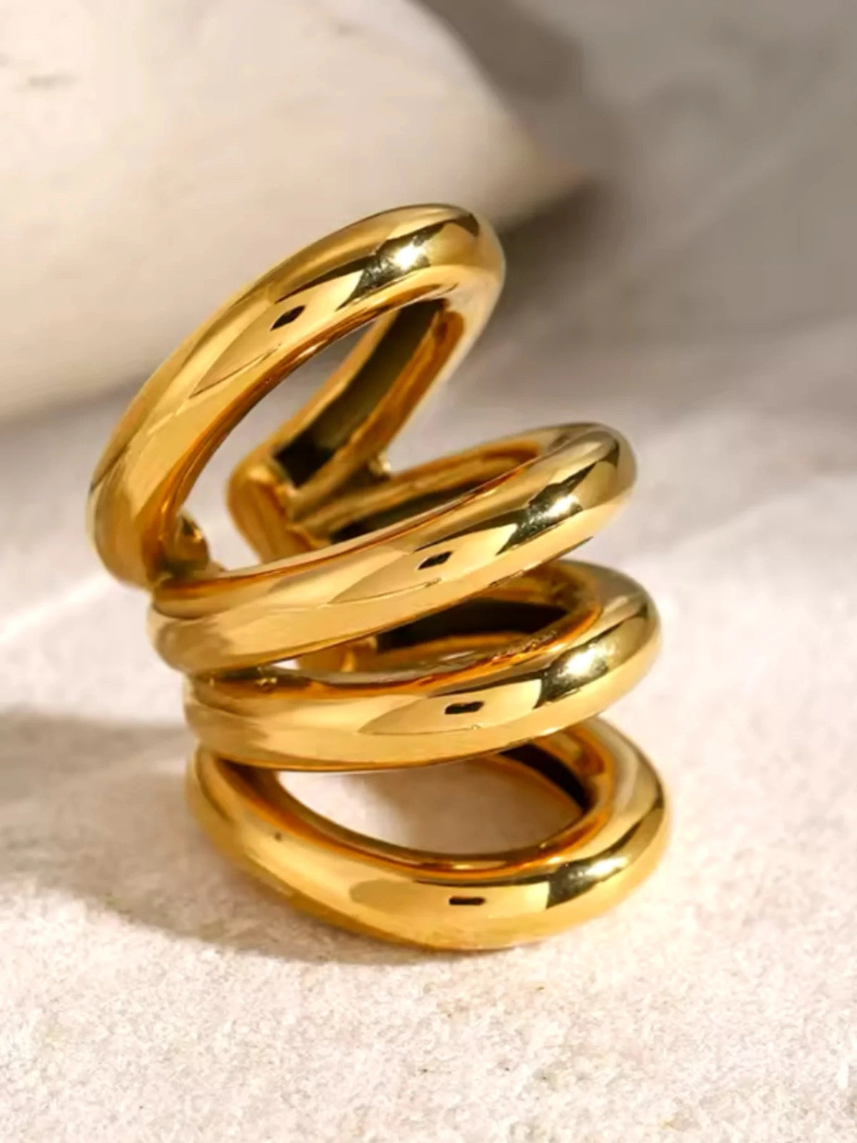 Faye Ear Cuff – Close‑Up Detail-Gold spiral ring on a textured beige surface