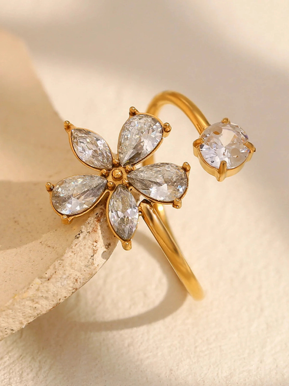 Flora Ring – Close-Up Detail-Gold earring with clear gemstones on a beige background