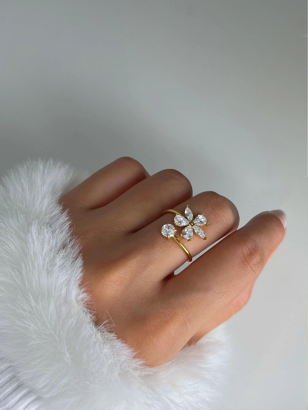 Flora Ring – Lifestyle Look-Hand wearing a gold ring with a floral design on a white fur surface