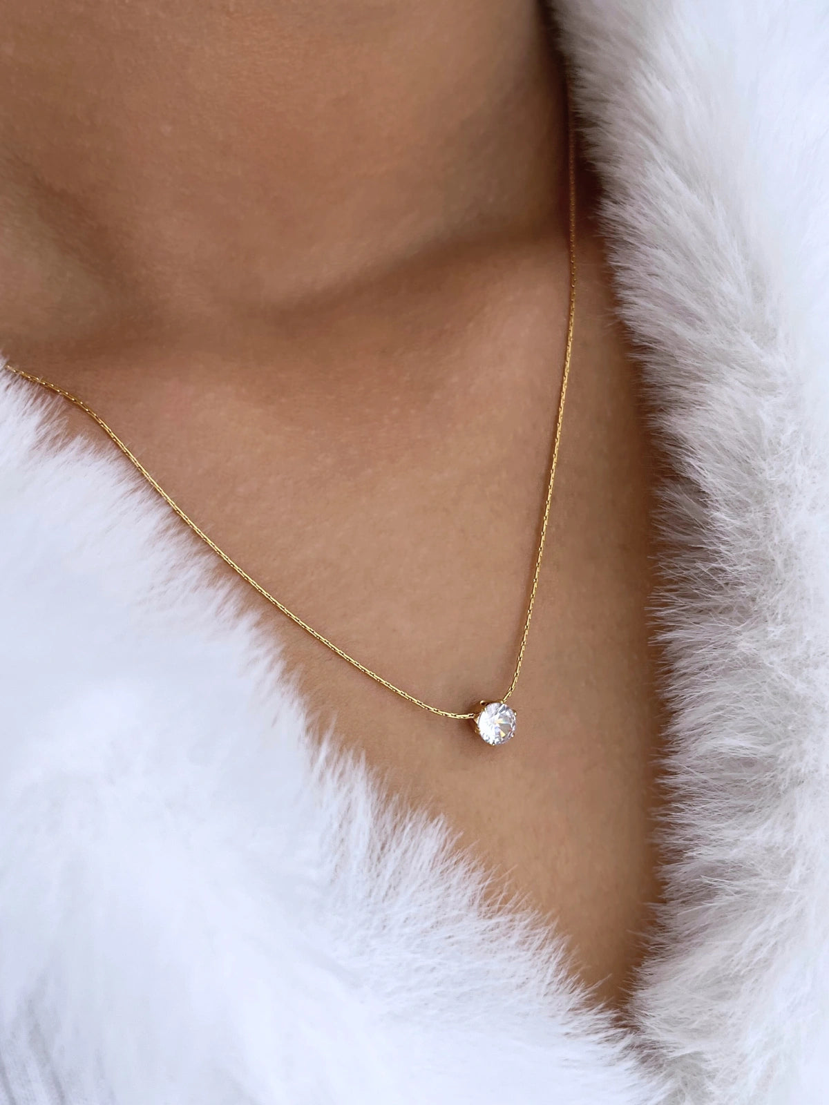 Glorien Necklace – On Model Styled Shot-Gold necklace with a heart pendant worn by a person in a white fur coat.