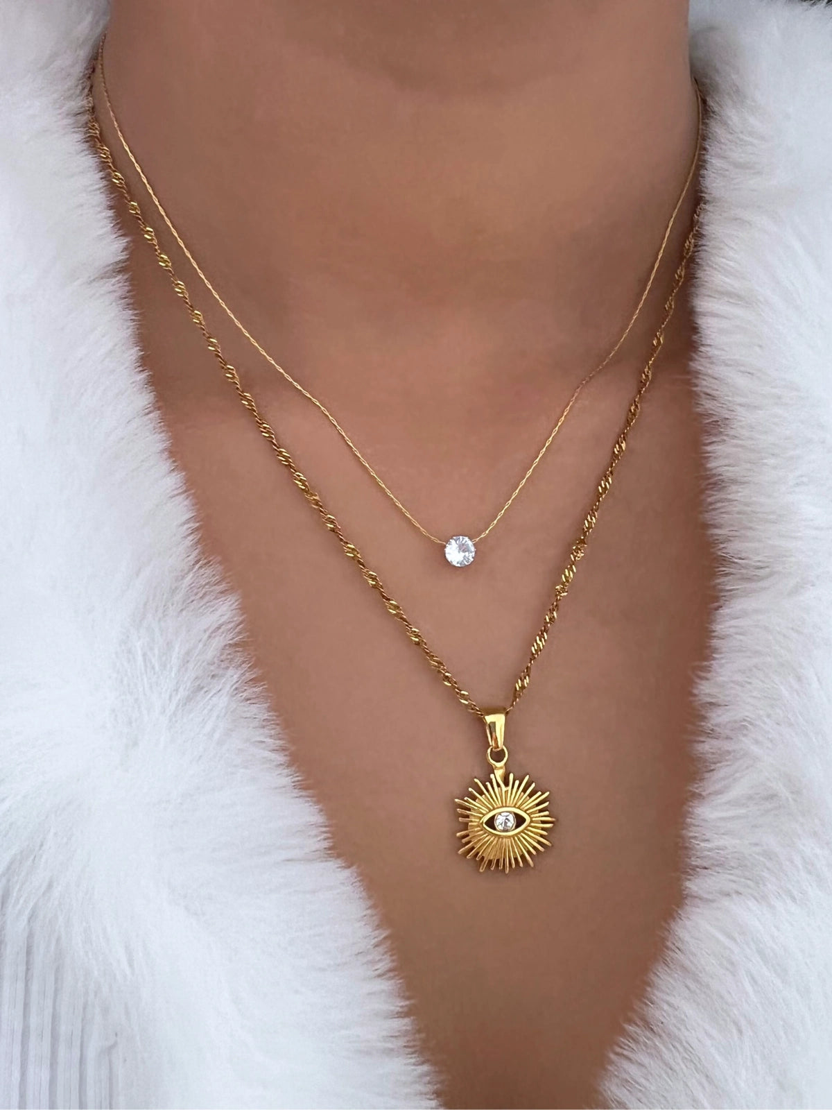 Glorien Necklace – On Model Styled Shot-Gold necklace with a sun pendant and small round pendant on a white fur background