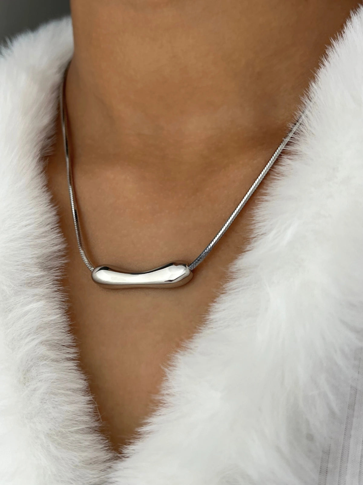 Halia Necklace – On Model Styled Shot-Silver necklace with a unique pendant on a person wearing a white fur coat.