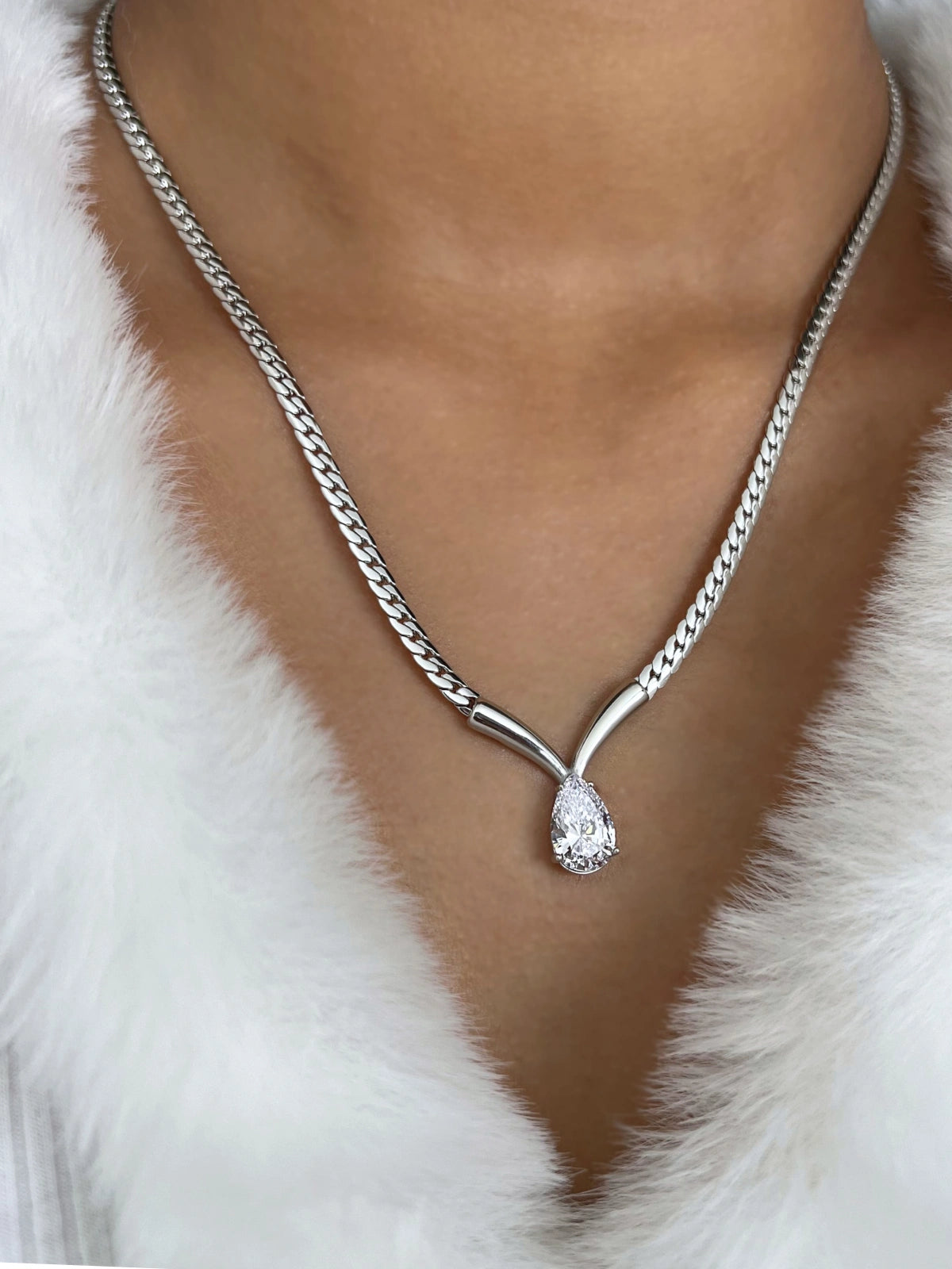 Imber Necklace – On Model Styled Shot-Silver necklace with a teardrop pendant on a person wearing a white fur garment.