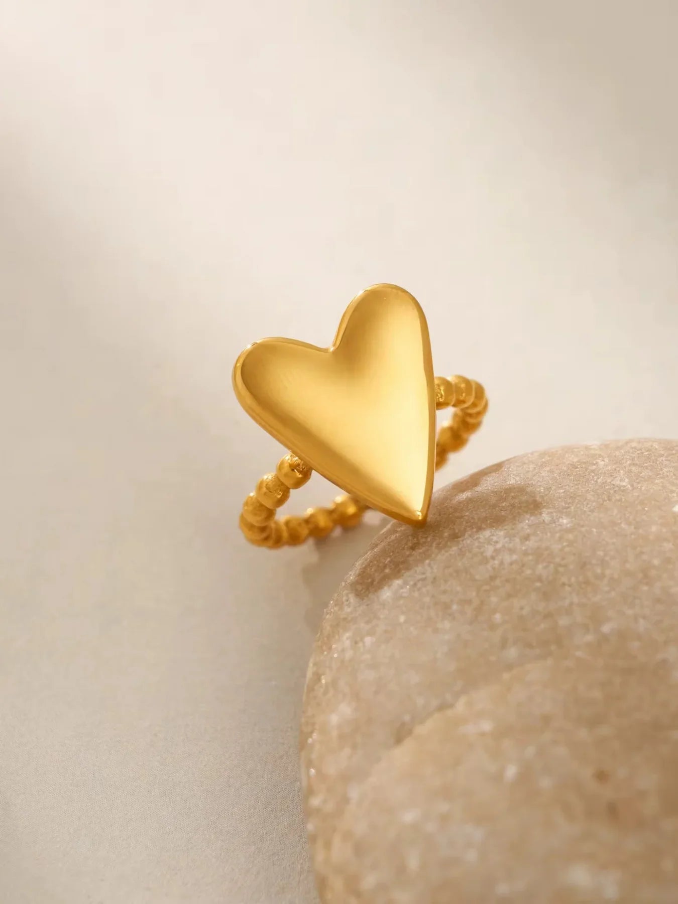 Love Vibe Ring – Close-Up Detail-Gold heart-shaped ring on a stone surface with a neutral background