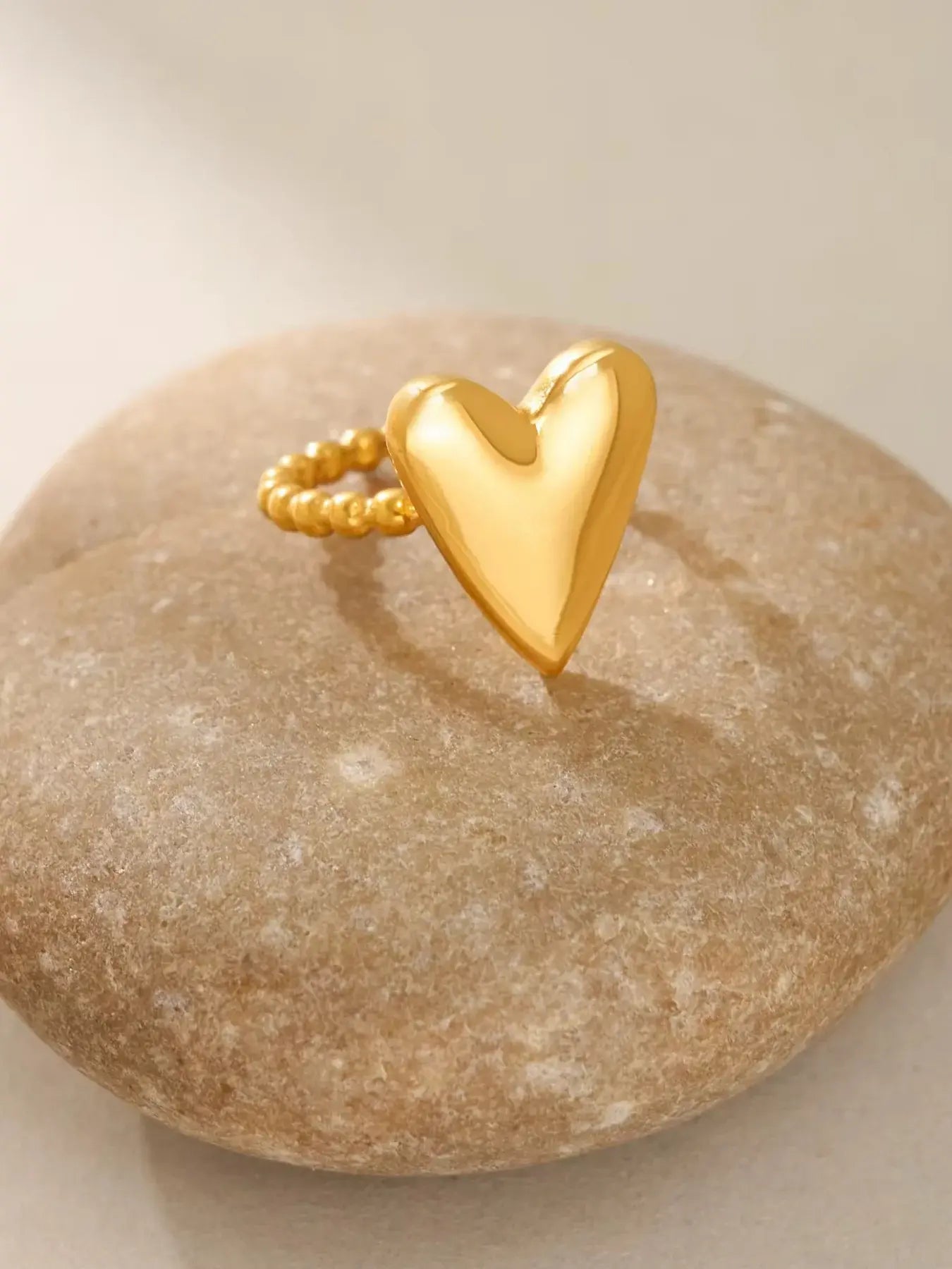 Love Vibe Ring – Close-Up Detail-Gold heart-shaped ring on a beige stone