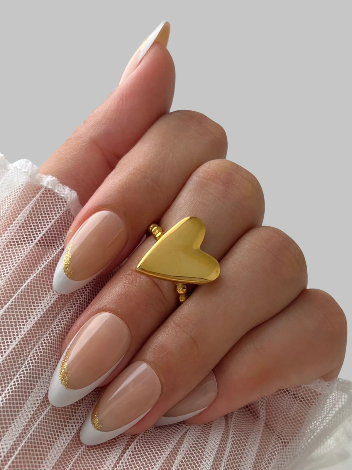 Love Vibe Ring – On Model Styled Shot-Hand wearing a gold heart-shaped ring with white and gold nail polish on a neutral background