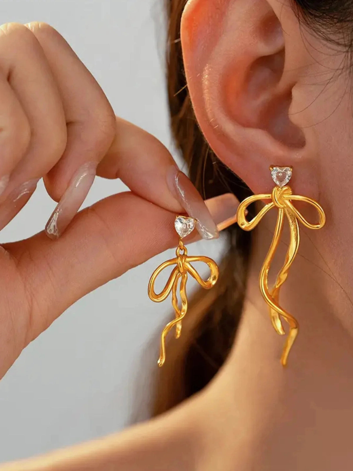 Lovella Bow Earring worn on ear — 18K gold‑plated stainless steel bow‑design by Shine With Me, styled look in pink.