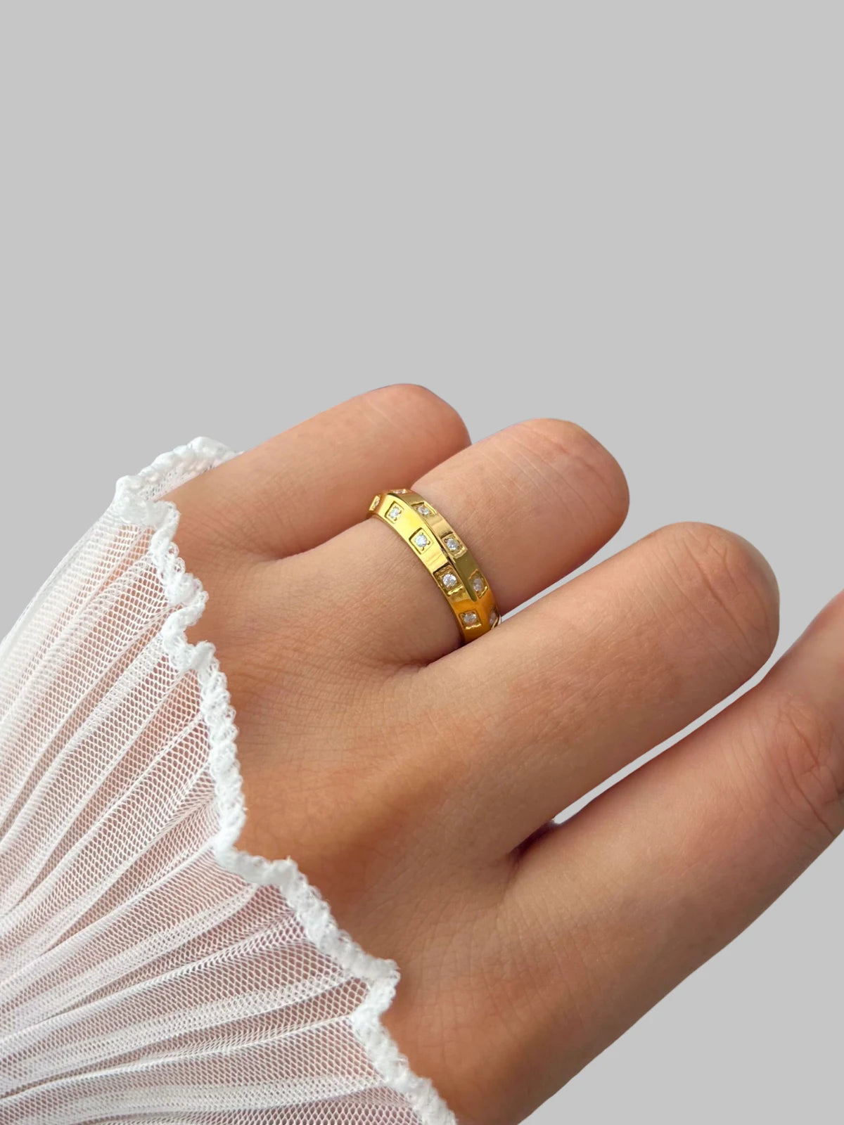 Lucena Ring – Worn on Finger-Gold ring on a finger with a white lace sleeve against a gray background