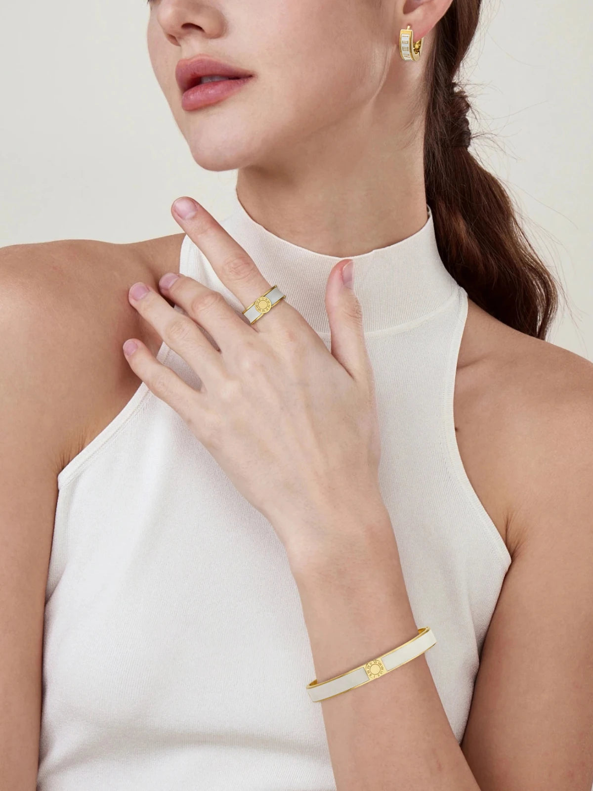 Lucia_Ring_Front_View. Woman wearing gold jewelry including a ring, bracelet, and earrings on a white background
