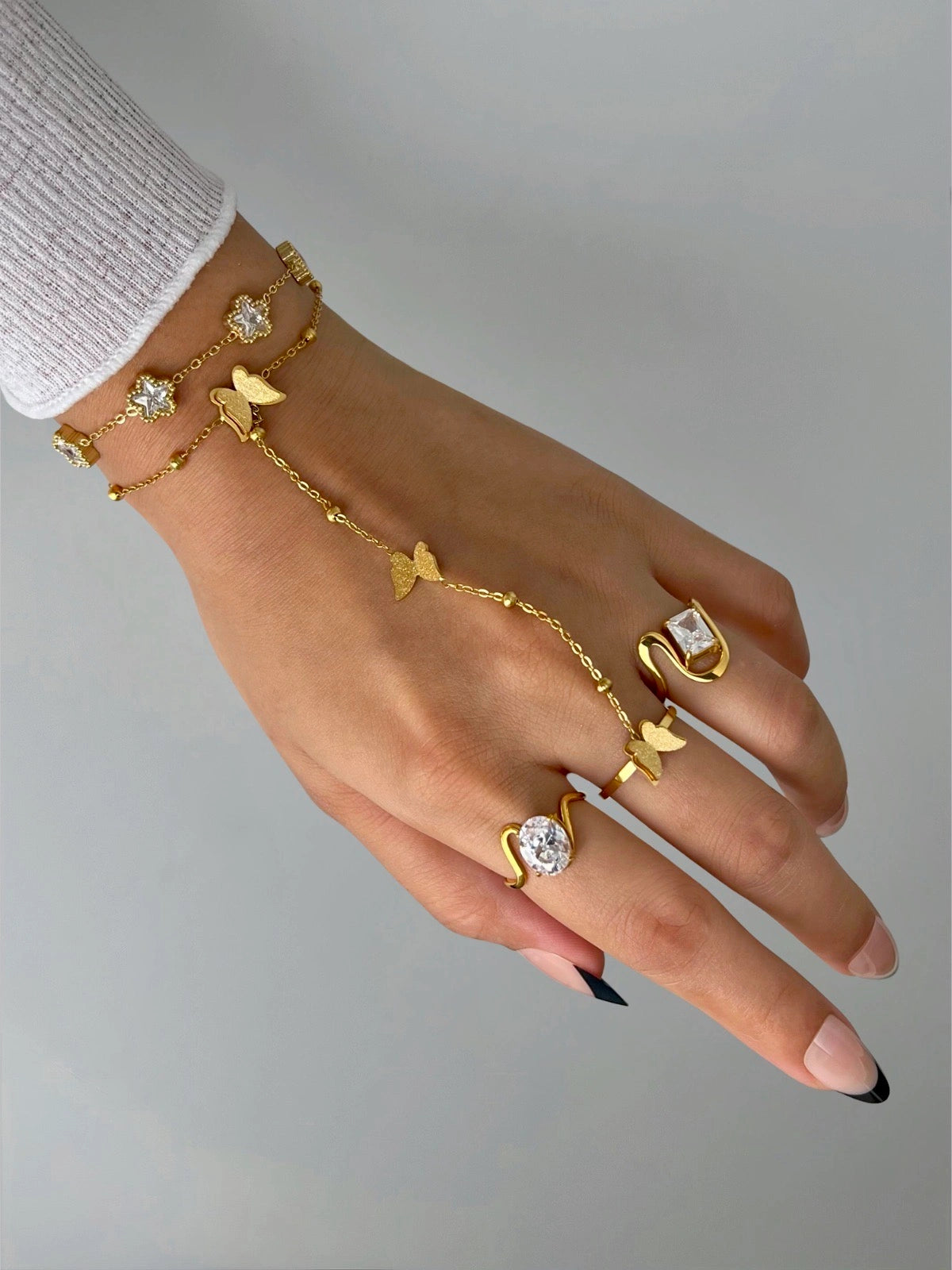 Lucie Rings – Worn on Finger-Hand wearing gold jewelry with rings and bracelets on a neutral background