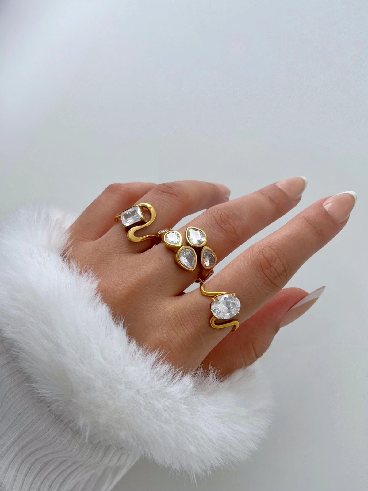Lucie Rings – Worn on Finger-Hand wearing gold rings with clear stones on a white background