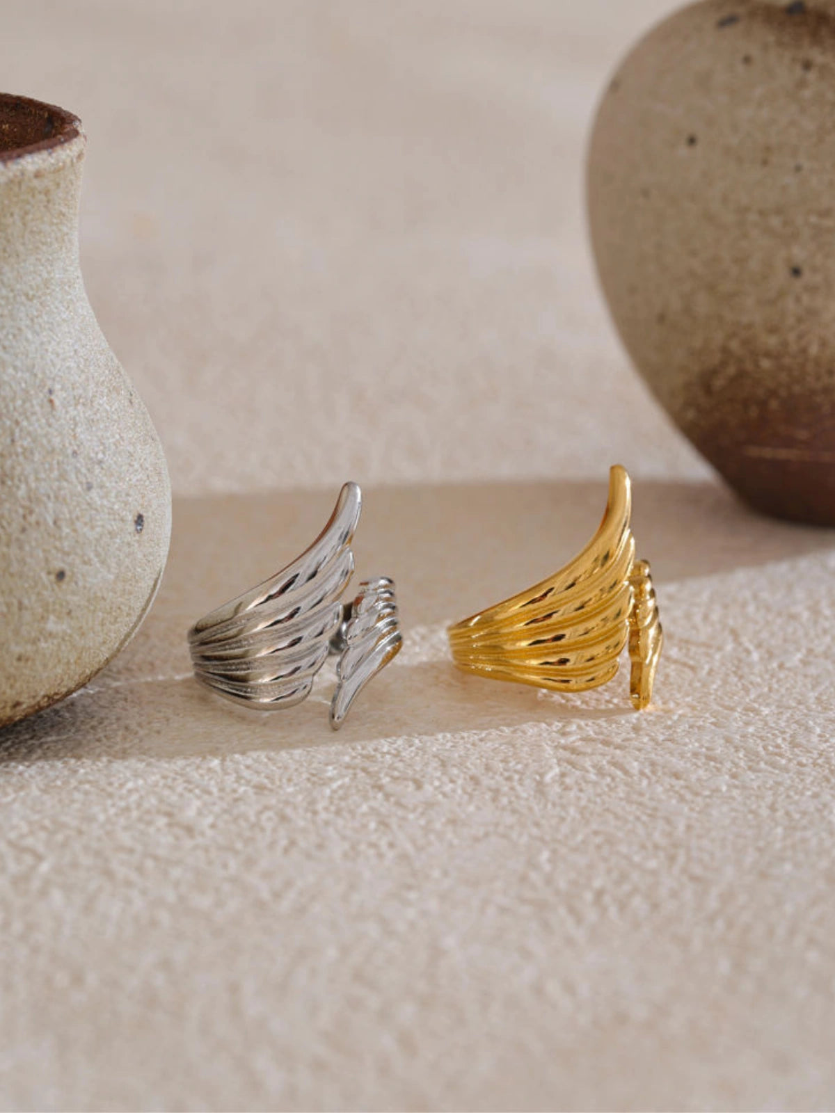 Luxe_Ring_Front_View_1Two rings, one silver and one gold, on a textured surface with ceramic vases in the background.