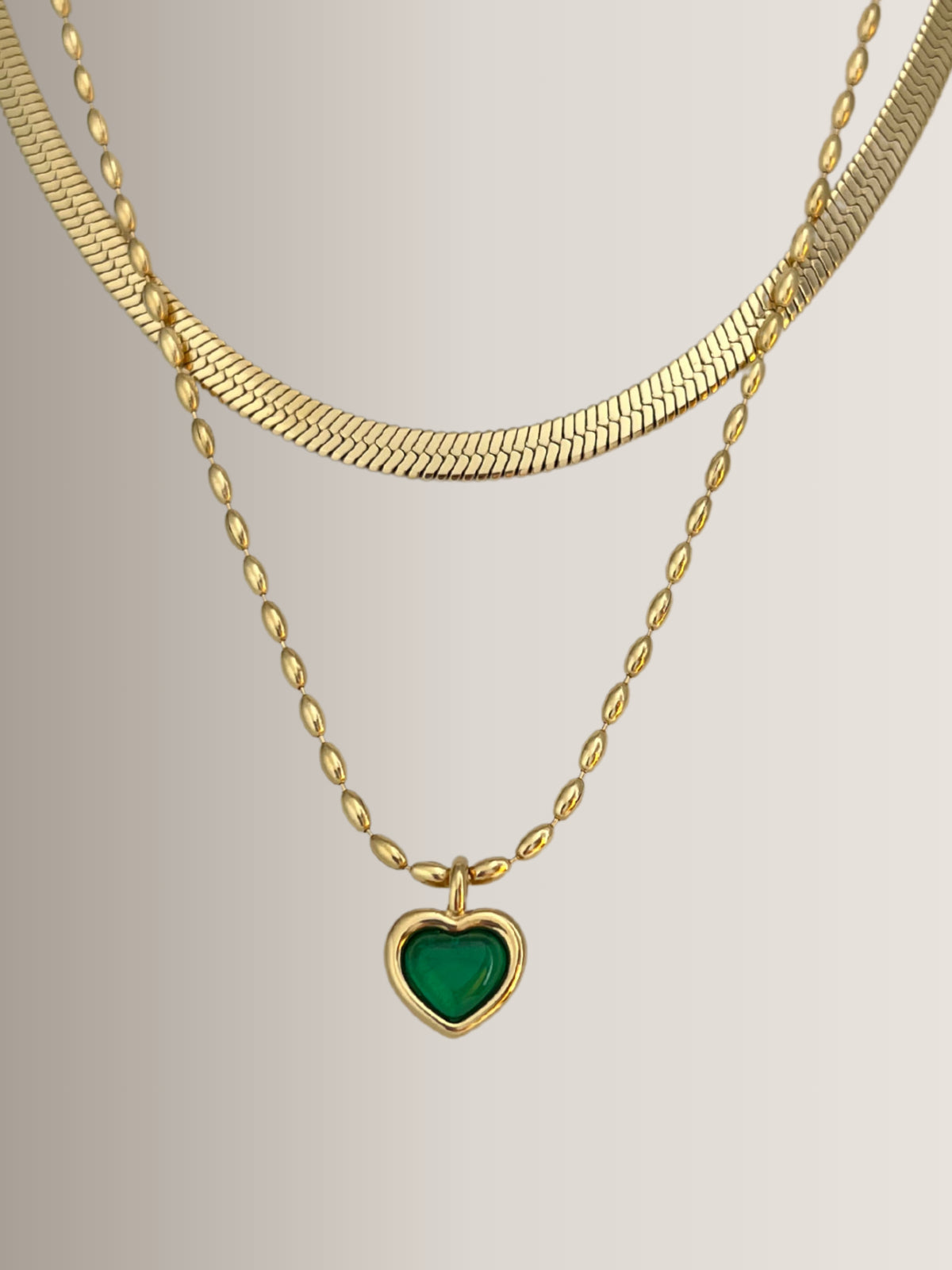 Lyra Heart Necklace – Close-Up Detail-Gold necklace with a green heart pendant on a light gray background