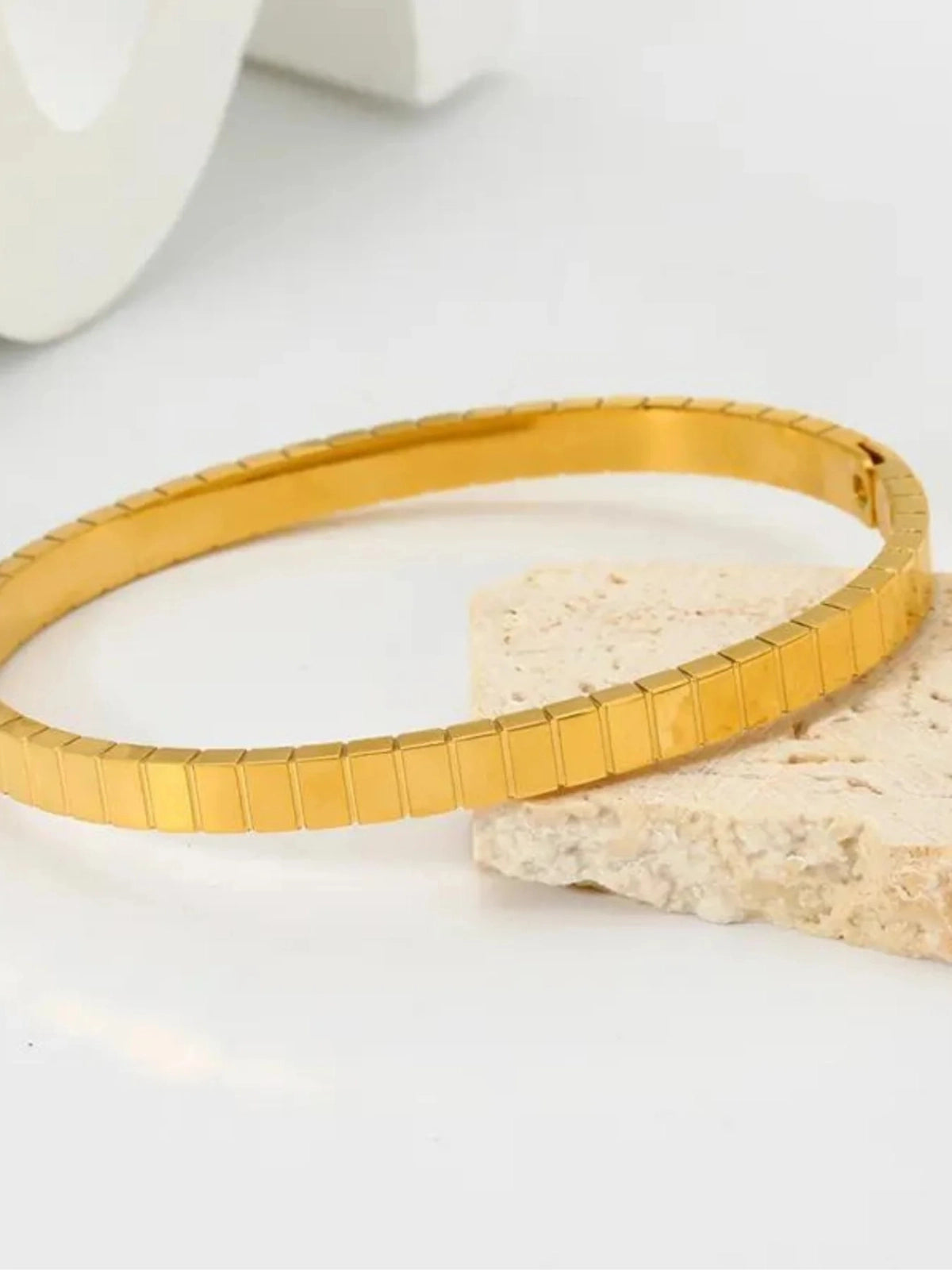 Mimi Bangle – Gold Variant, Gold bracelet on a light surface with a neutral background