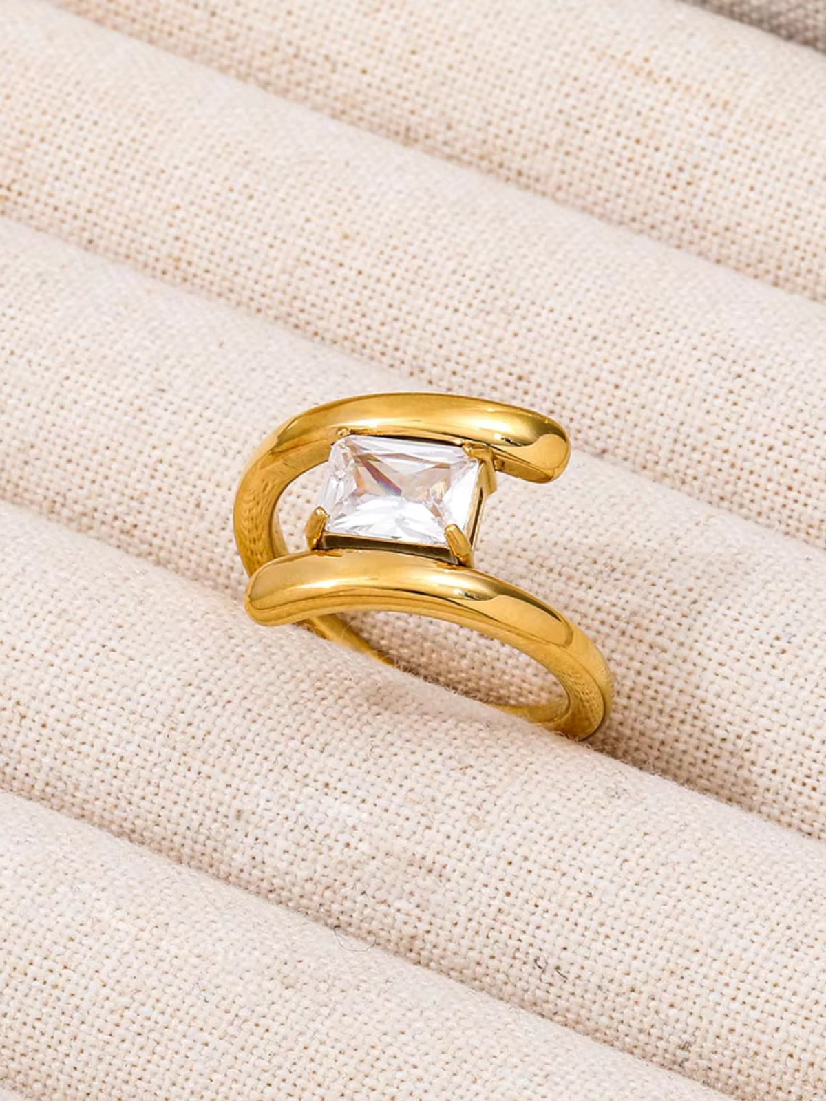 Moonbeam_Ring_Front_View_1Gold ring with a clear gemstone on a beige fabric background