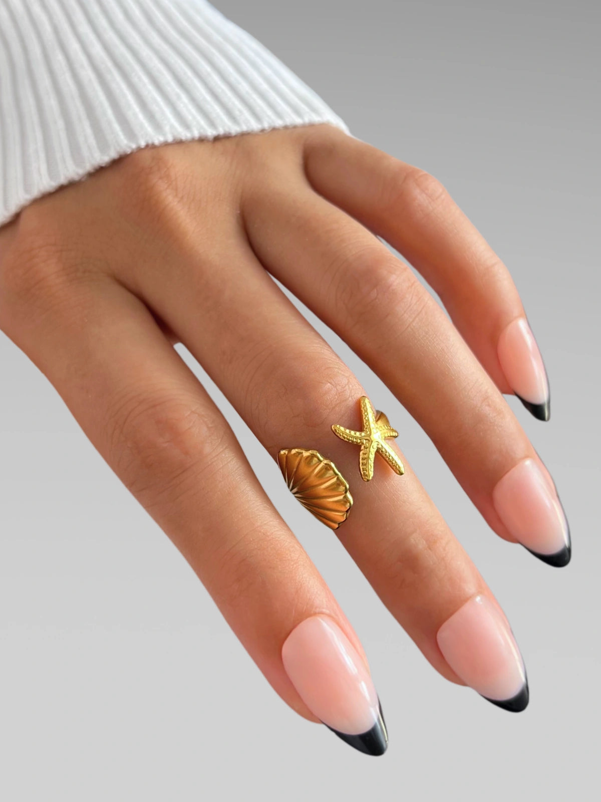 Ocean Embrace Ring Hand wearing two gold rings with a gray background