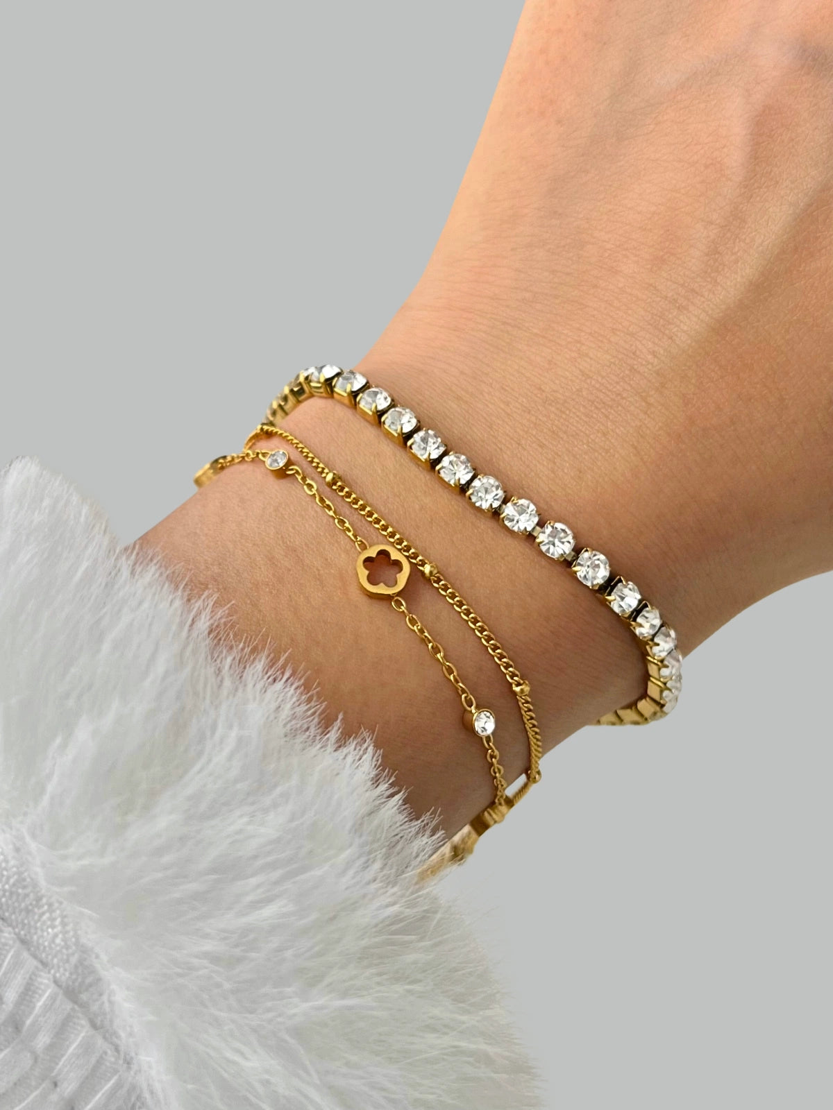 iva Flower Bracelet – On Wrist, Close-up of a wrist wearing multiple gold and silver bracelets on a light gray background.