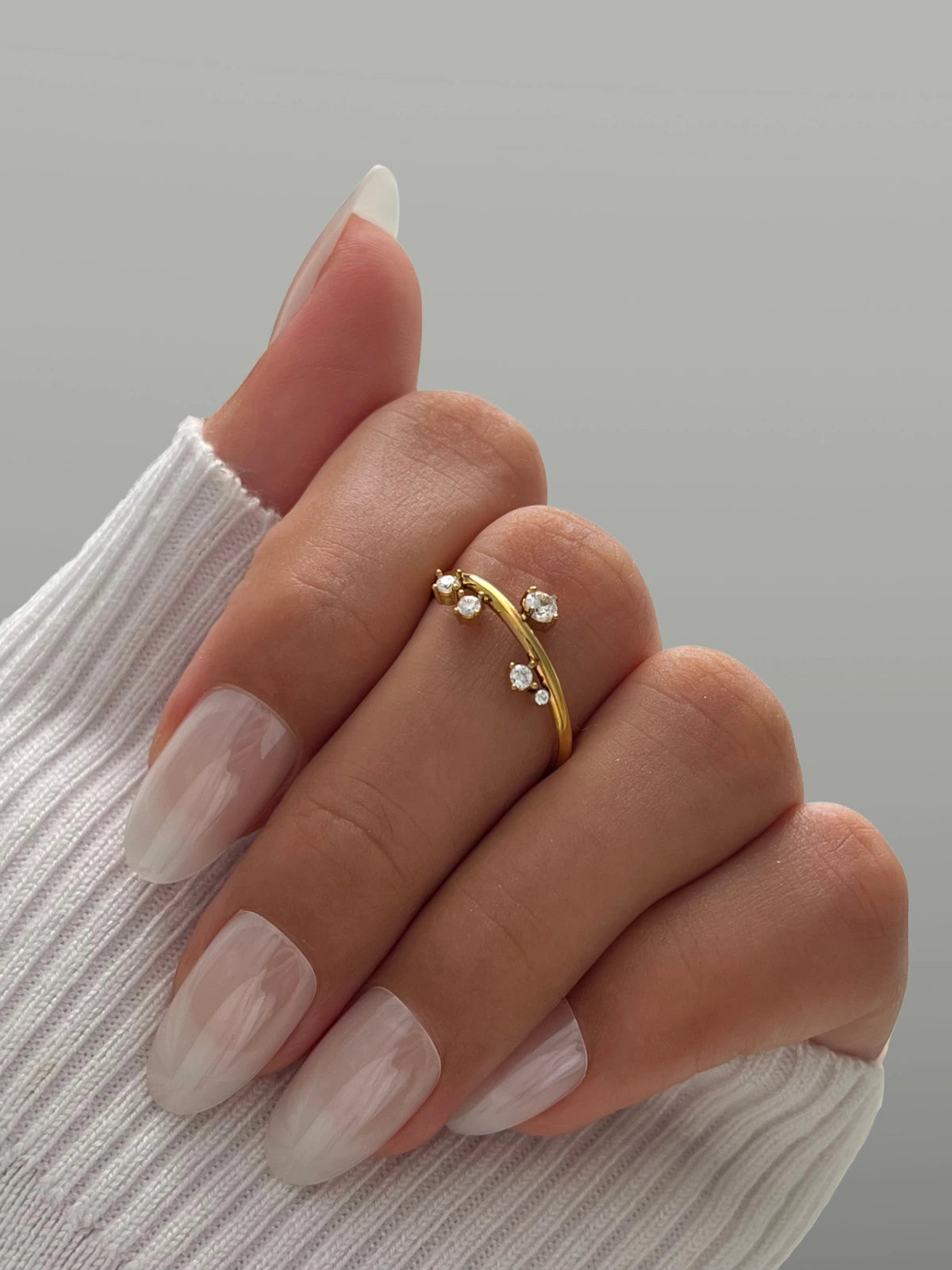 Sandrine Ring – Worn on Finger-Gold ring with small diamonds on a hand with light nail polish against a neutral background