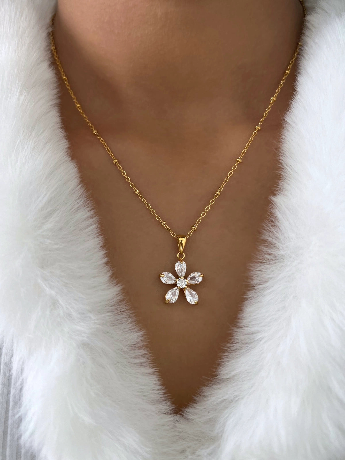 Solea Necklace – On Model Styled Shot-Gold necklace with a floral pendant on a white fur background
