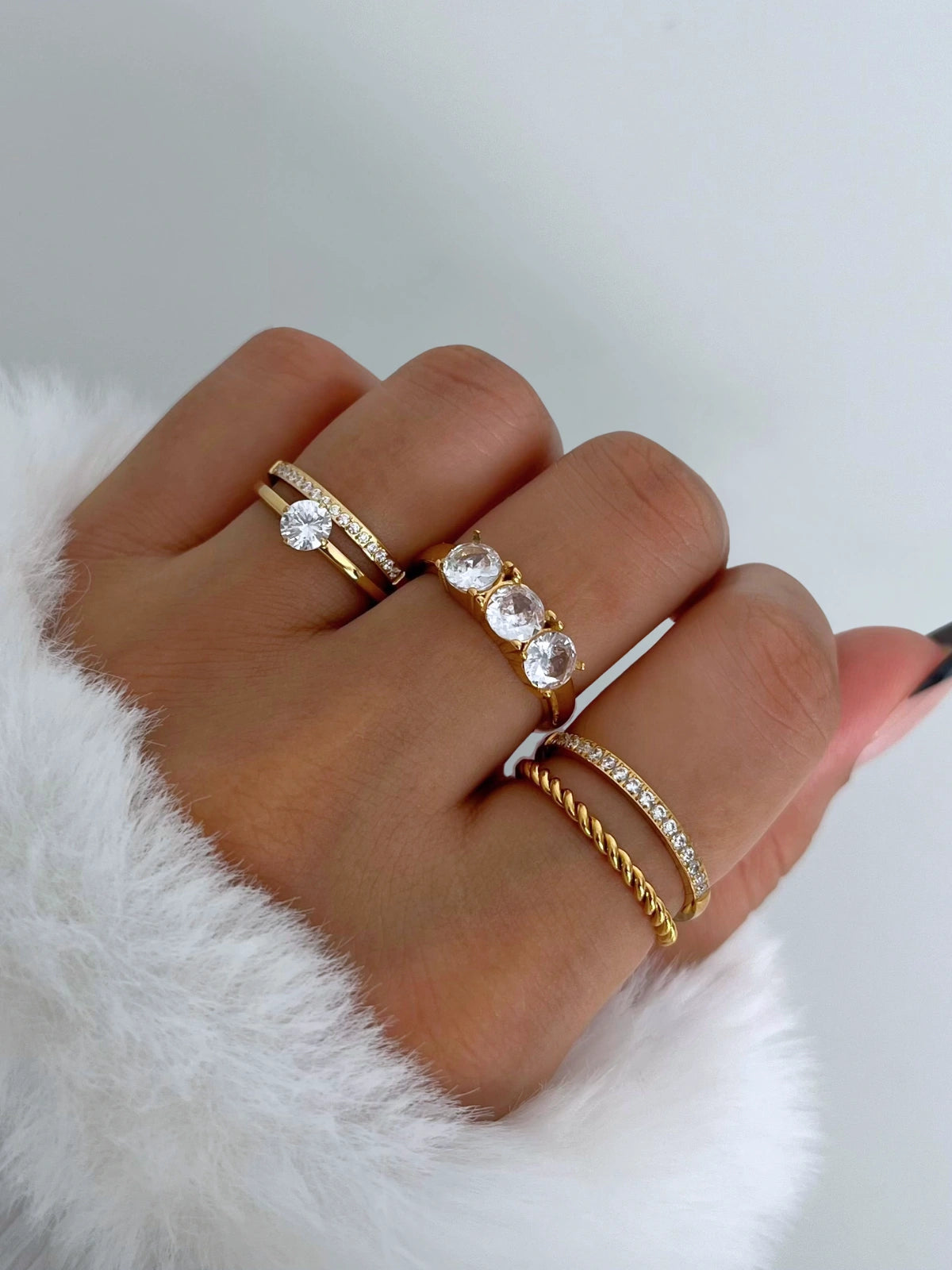 Sophisticate Ring – Worn on Finger-Close-up of a hand wearing multiple gold and diamond rings on a white background