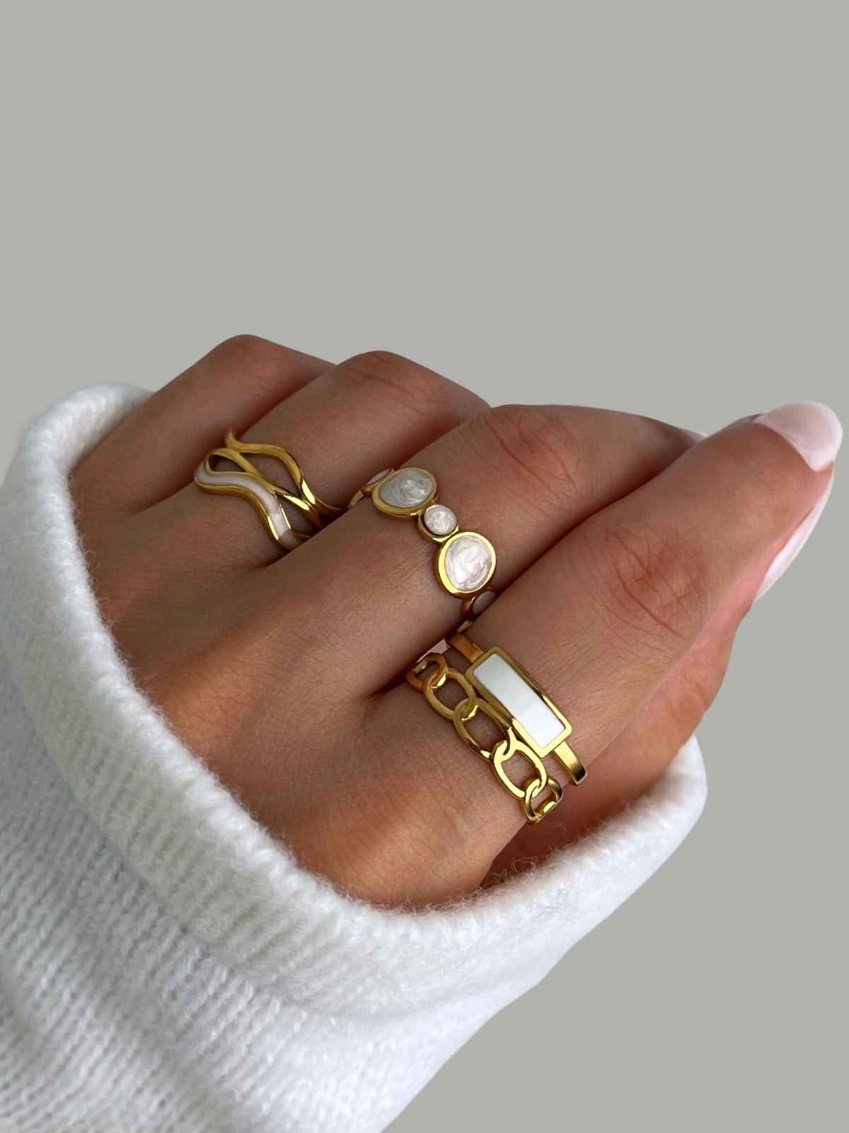 Sozi RINGS-Hand wearing multiple gold rings on a neutral background