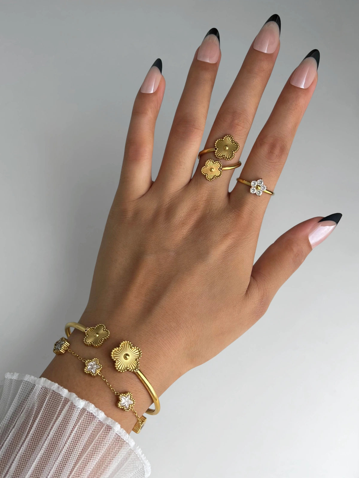 Sunveil Bangle and Hand wearing gold rings and bracelet with black and pink nail polish on a neutral background
