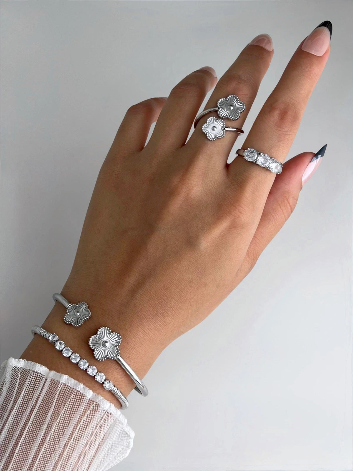 Sunveil Bangle, Hand wearing silver floral ring and bracelet on a plain background