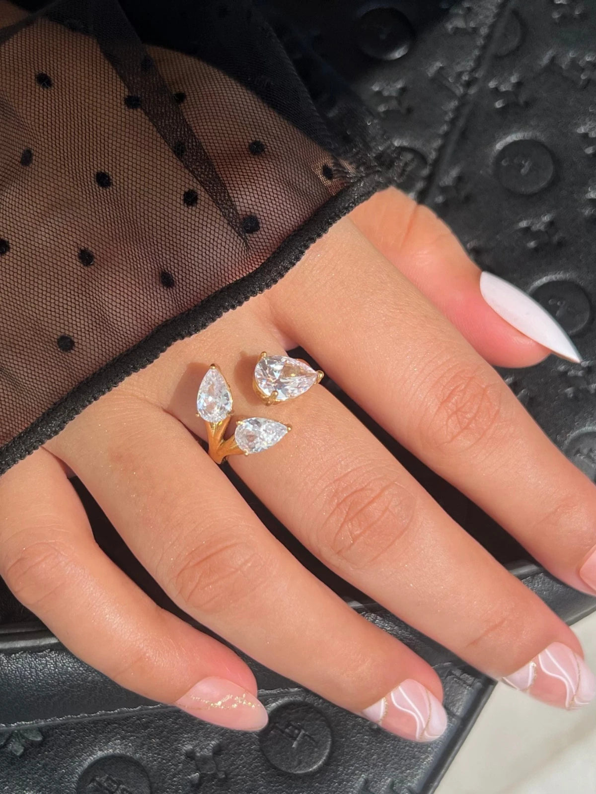 The Astria Ring – On Model Styled Shot-Close-up of a hand wearing a diamond ring on a textured black surface
