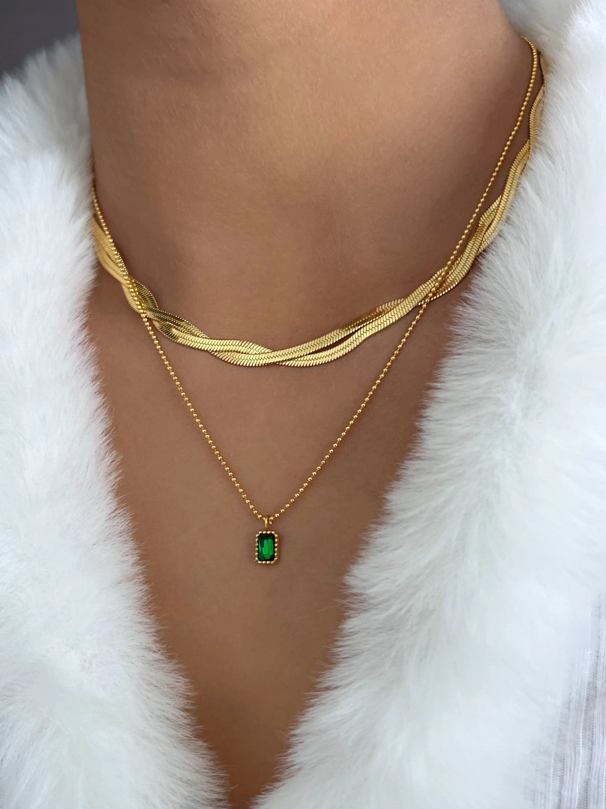 Twinwave Chain – On Model Styled Shot-Gold necklace with a green gemstone on a white fur background