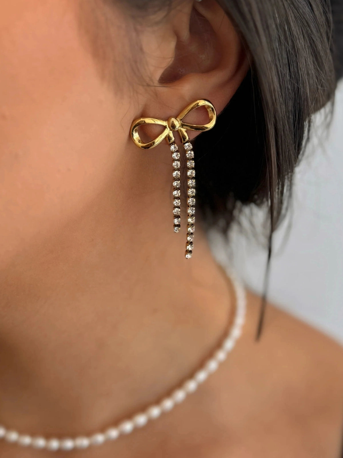 Valentina Bow Earring – Side View, Gold bow-shaped earring with rhinestones worn by a person.