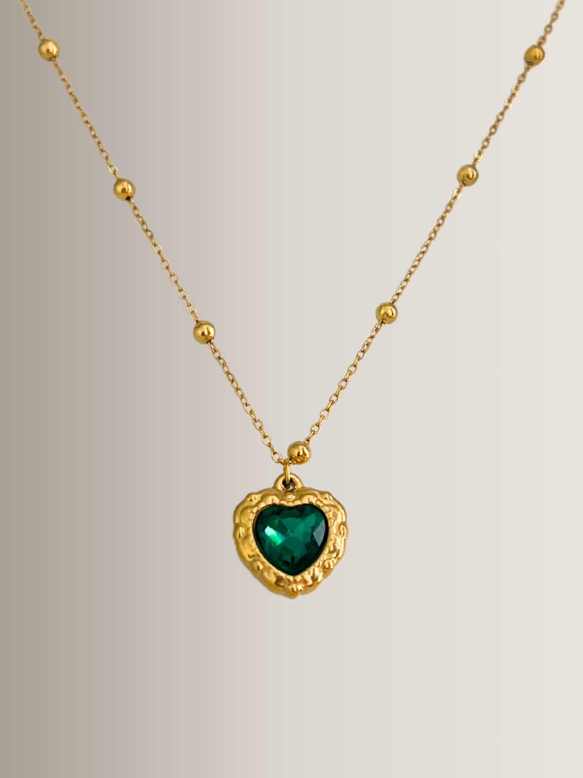 Zafira Necklace – Close‑Up Detail-Gold necklace with a heart-shaped green gemstone pendant on a light gray background
