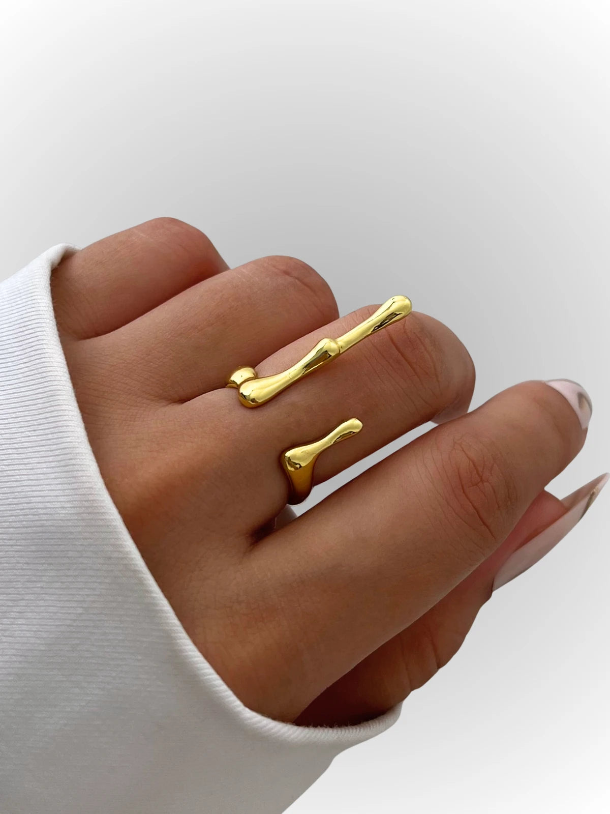 aqua-ring-closeup-detail-shine-with-me Gold bone-shaped rings on a hand against a white background