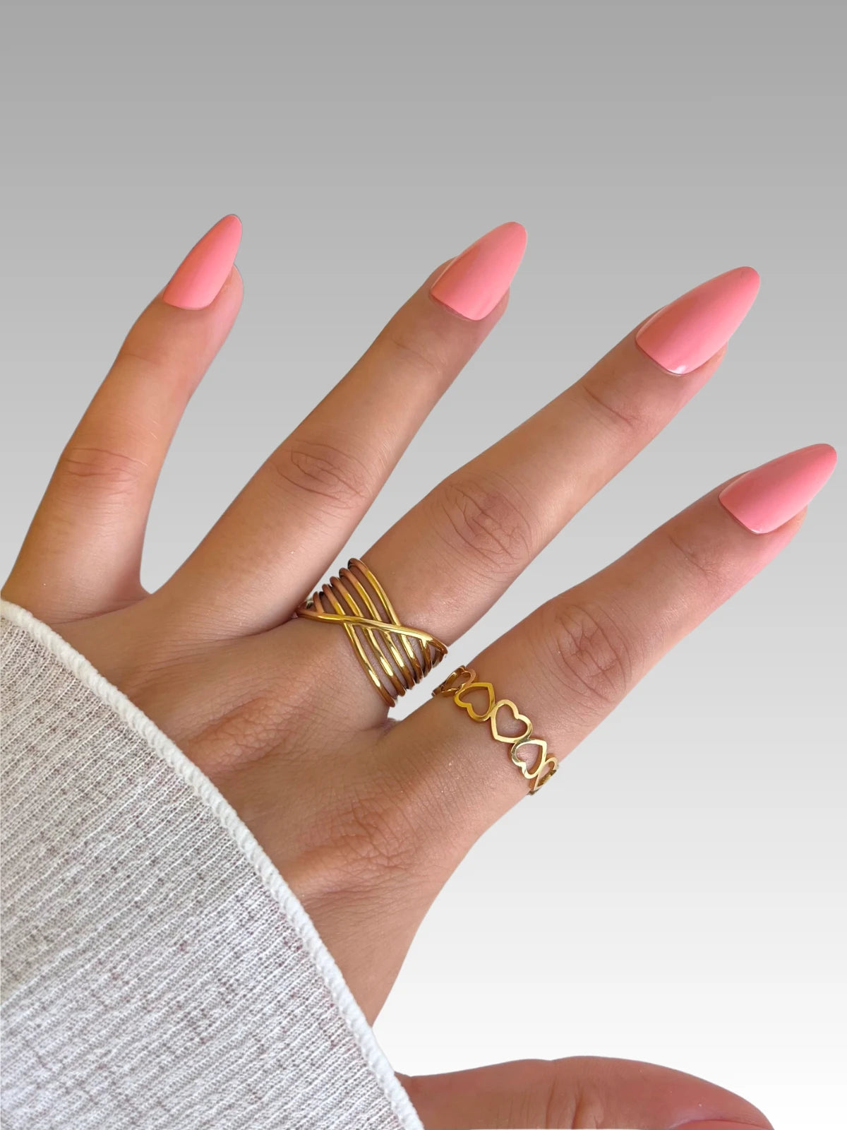 daily-rings-closeup-detail-shine-with-me Hand with pink nail polish wearing gold rings on a neutral background
