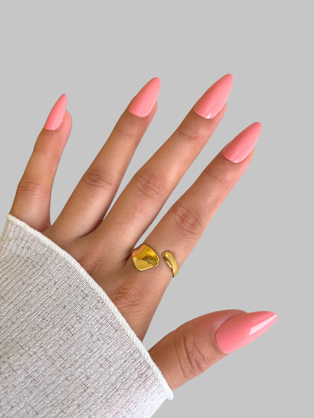daily-rings-closeup-detail-shine-with-me Hand with pink nails wearing a gold ring on a gray background