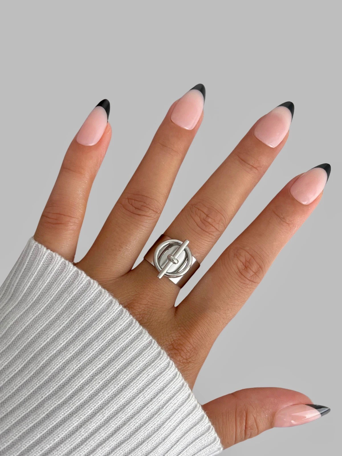 dorian-belt-ring-closeup-detail-shine-with-me Hand wearing a silver ring with a gray background