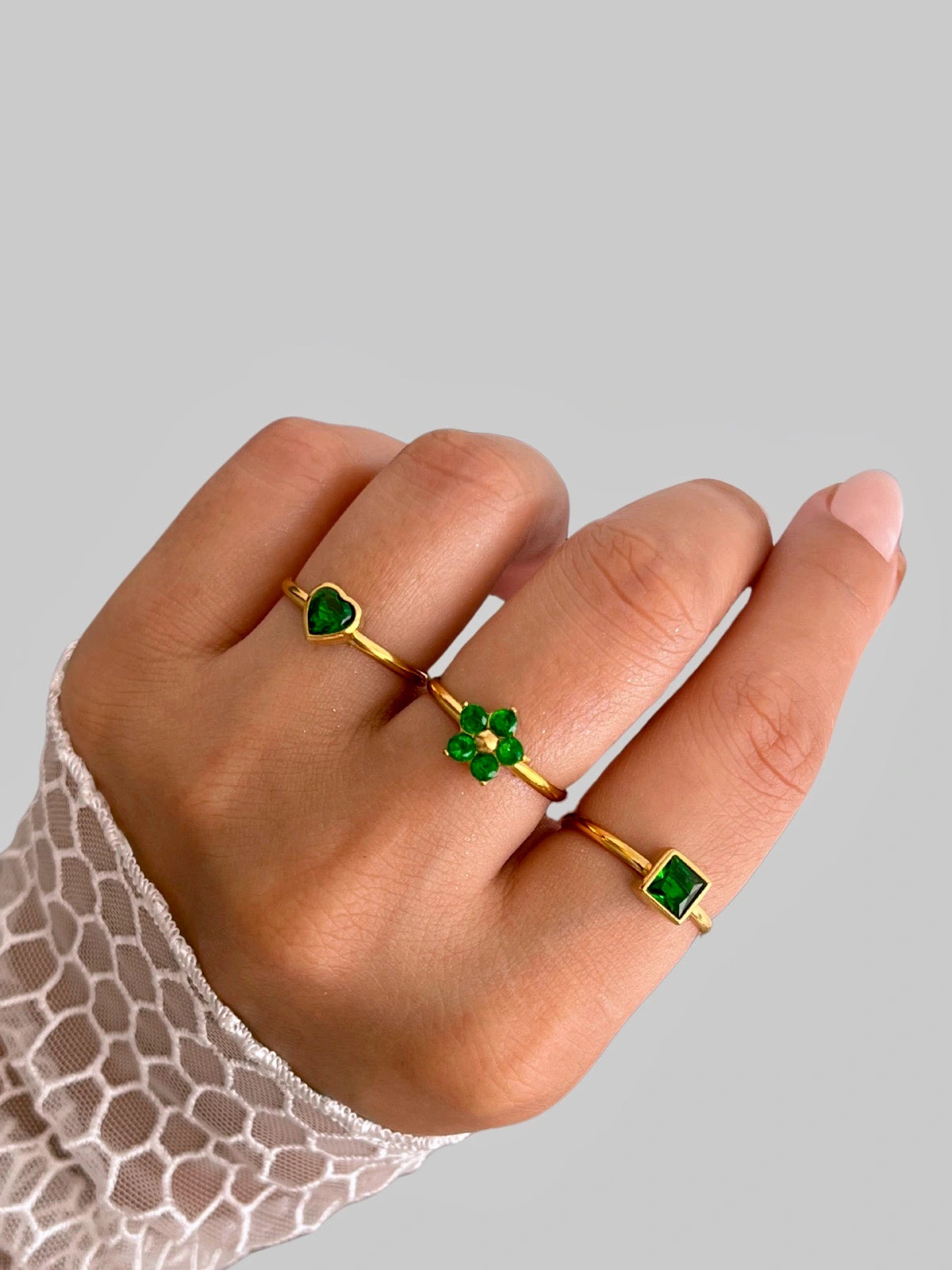 dua-ring-side-angle-shine-with-me-Hand wearing three gold rings with green gemstones on a gray background
