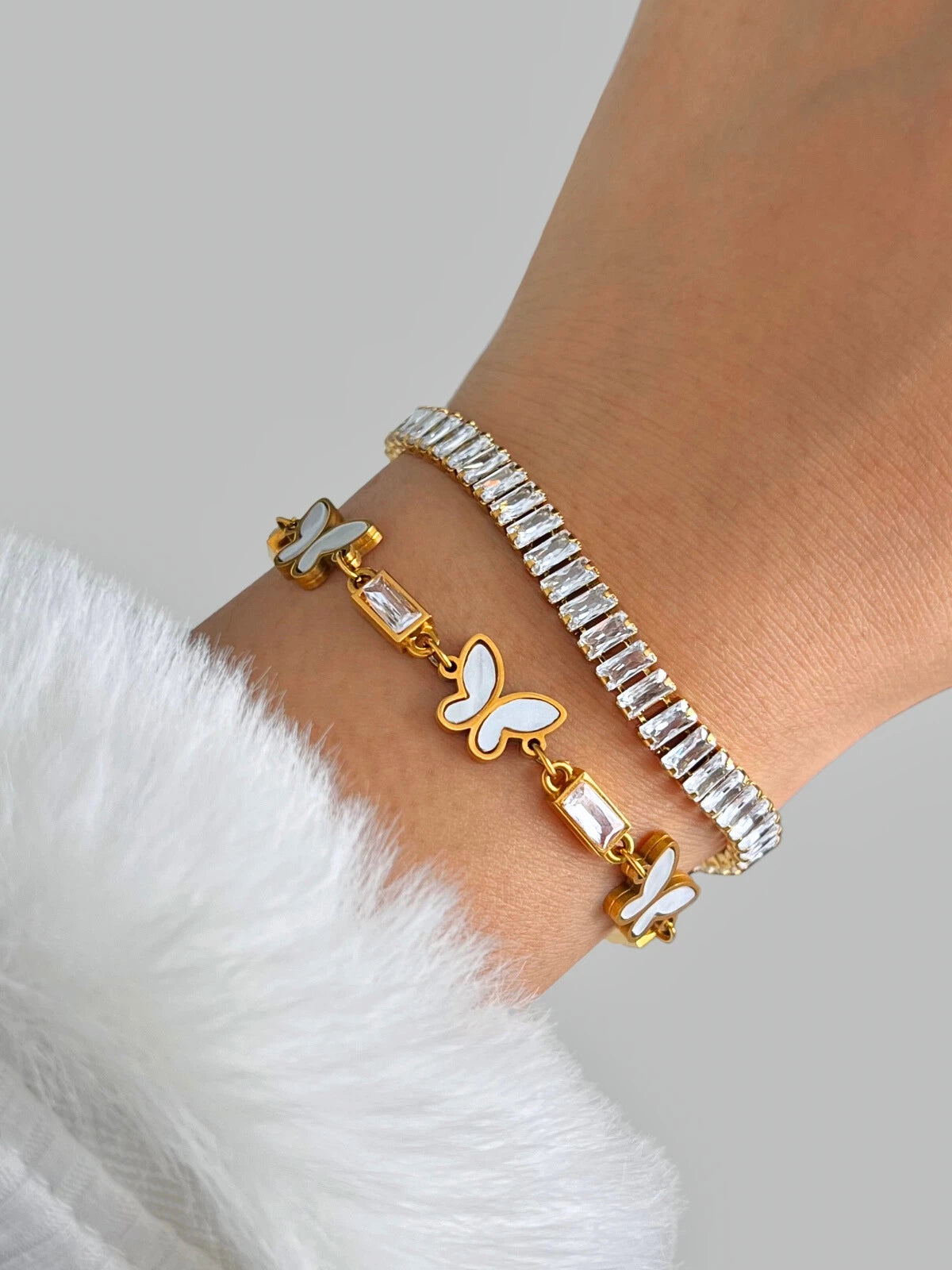lly Bracelet – Close-Up Detail. Two bracelets with butterfly charms on a wrist against a white background