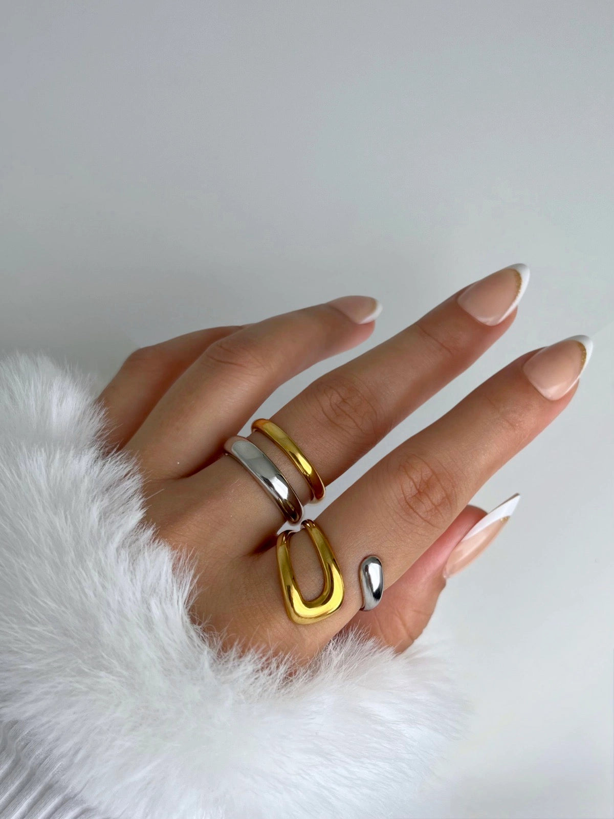 seaborn-ring-side-angle-shine-with-me Hand wearing three rings on a white fur surface