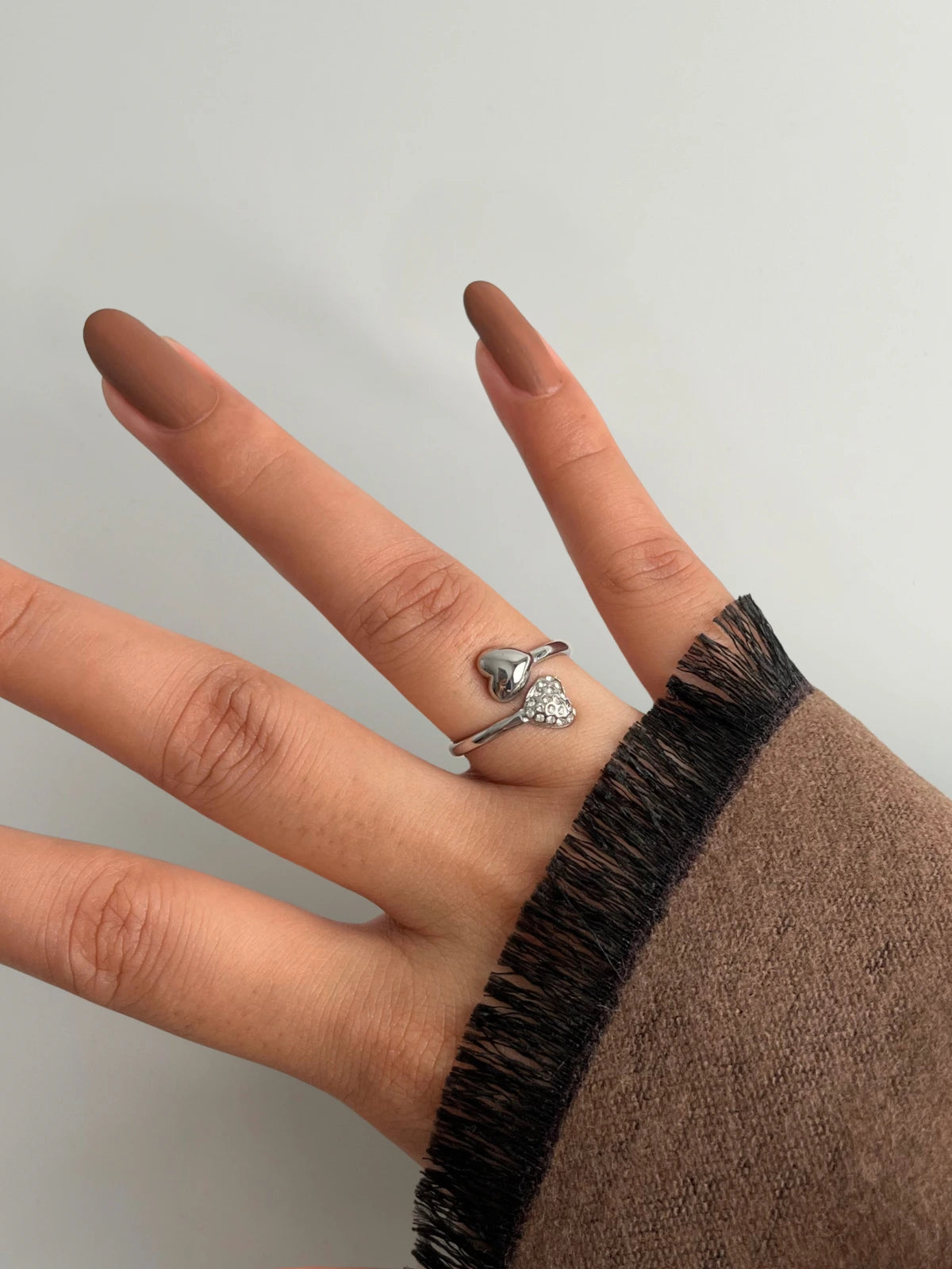 us-together-ring-closeup-detail-shine-with-me Hand wearing a silver ring with a clear gemstone on a plain background