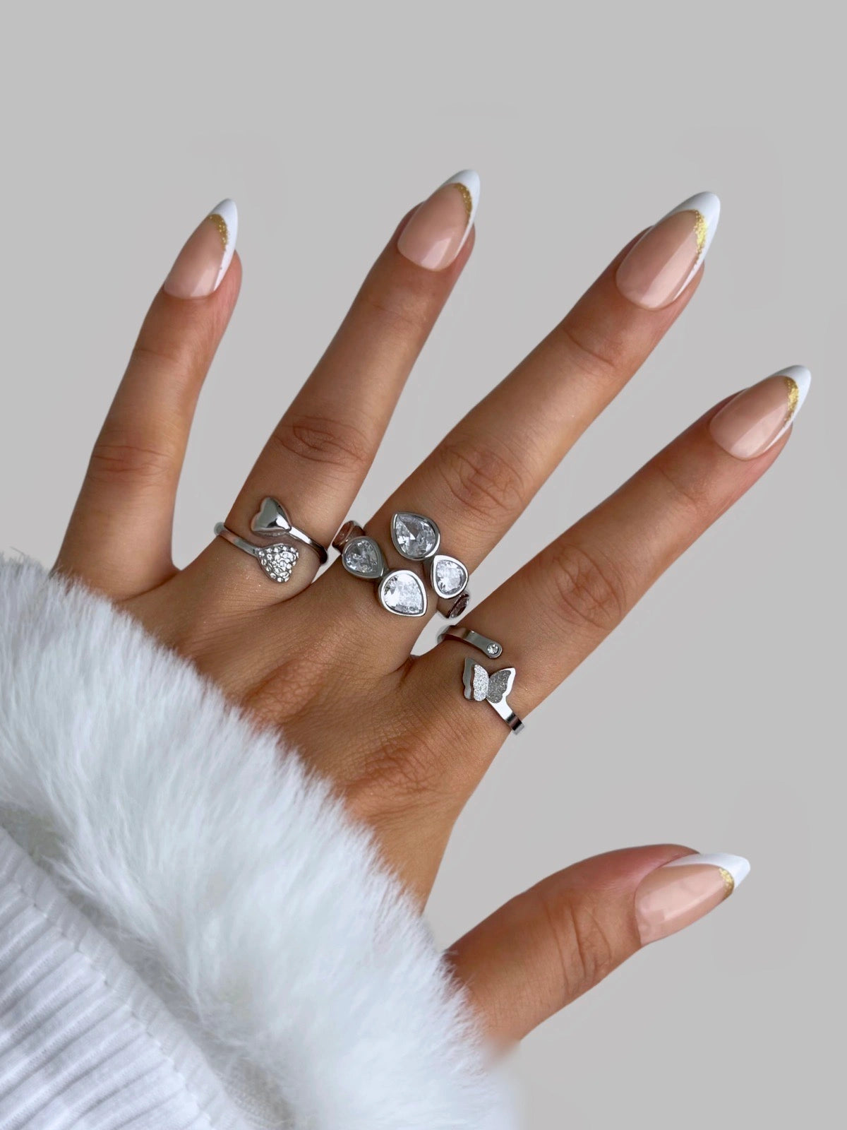 us-together-ring-closeup-detail-shine-with-me Hand wearing multiple silver rings with a neutral background